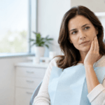 Woman holding her cheek while discussing tooth pain with a dentist when is a toothache an emergency