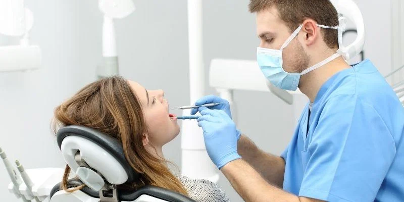 Masked dental professional checking a patient’s mouth