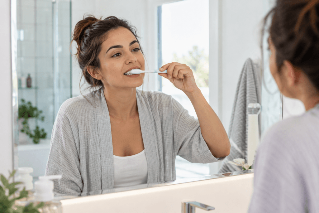 Adult brushing her teeth at a bathroom mirror